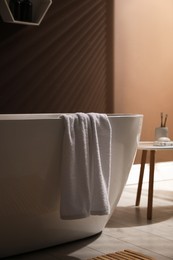 Modern ceramic bathtub with towel near brown wall indoors