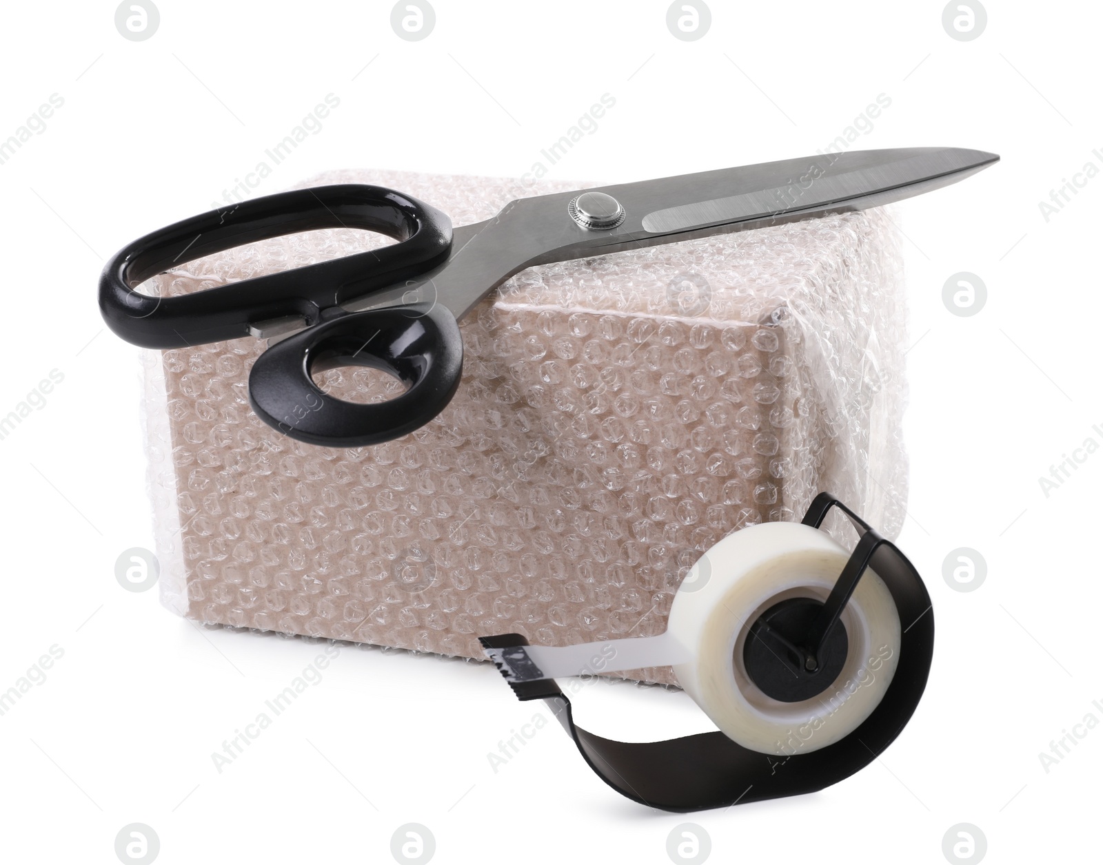 Photo of Cardboard box packed in bubble wrap, scissors and adhesive tape on white background