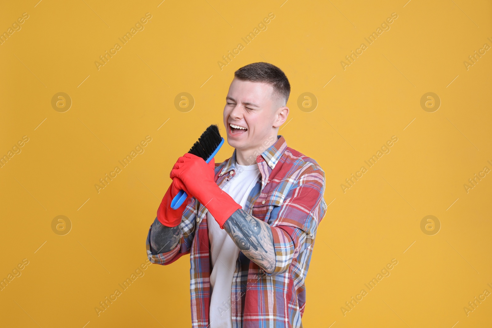 Photo of Handsome young man with brush singing on orange background