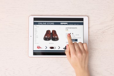 Woman with tablet shopping online at white wooden table, top view