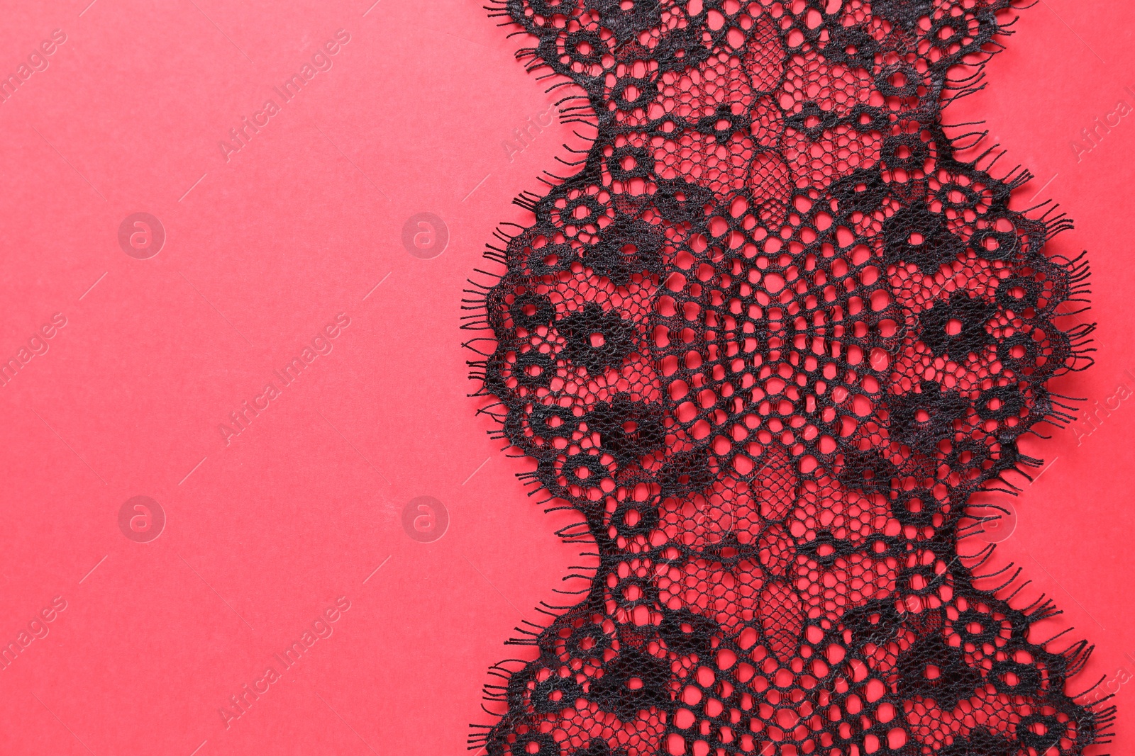 Photo of Black lace on red background, top view. Space for text