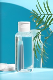 Bottle of micellar water, houseplant and cotton pads on light blue background near mirror