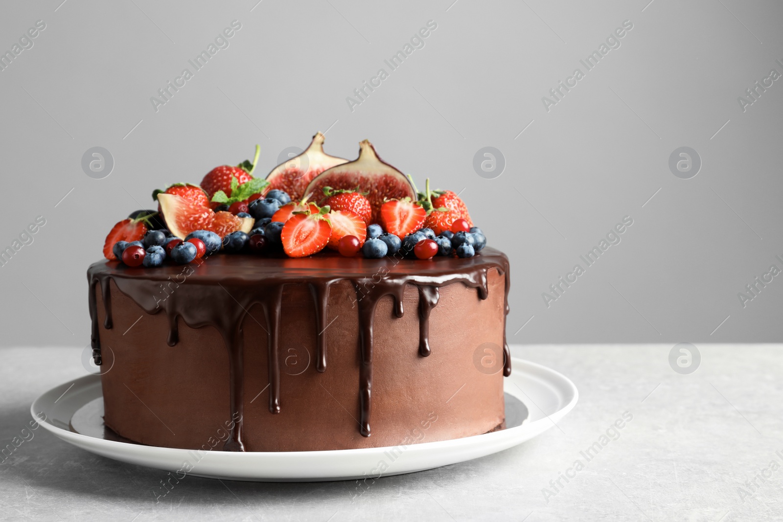 Photo of Fresh delicious homemade chocolate cake with berries on table against gray background