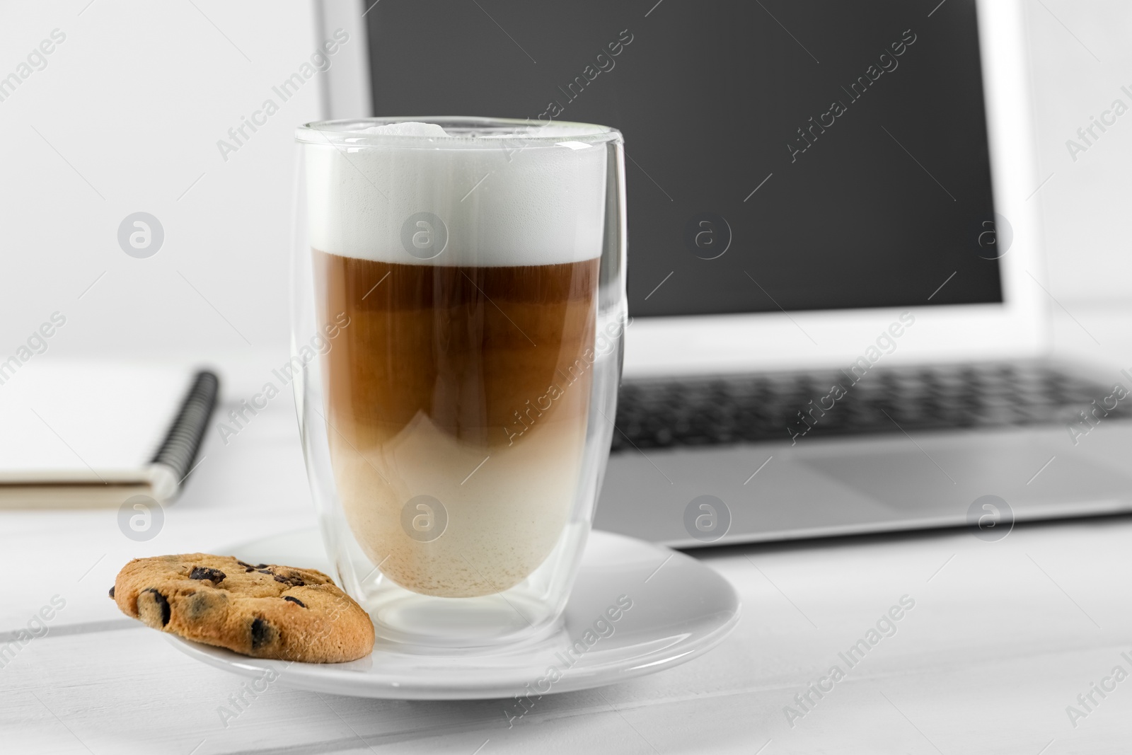 Photo of Chocolate chip cookie, latte and laptop on white wooden table indoors