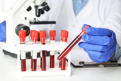 Photo of Scientist holding test tube with blood sample at table, closeup. Virus research