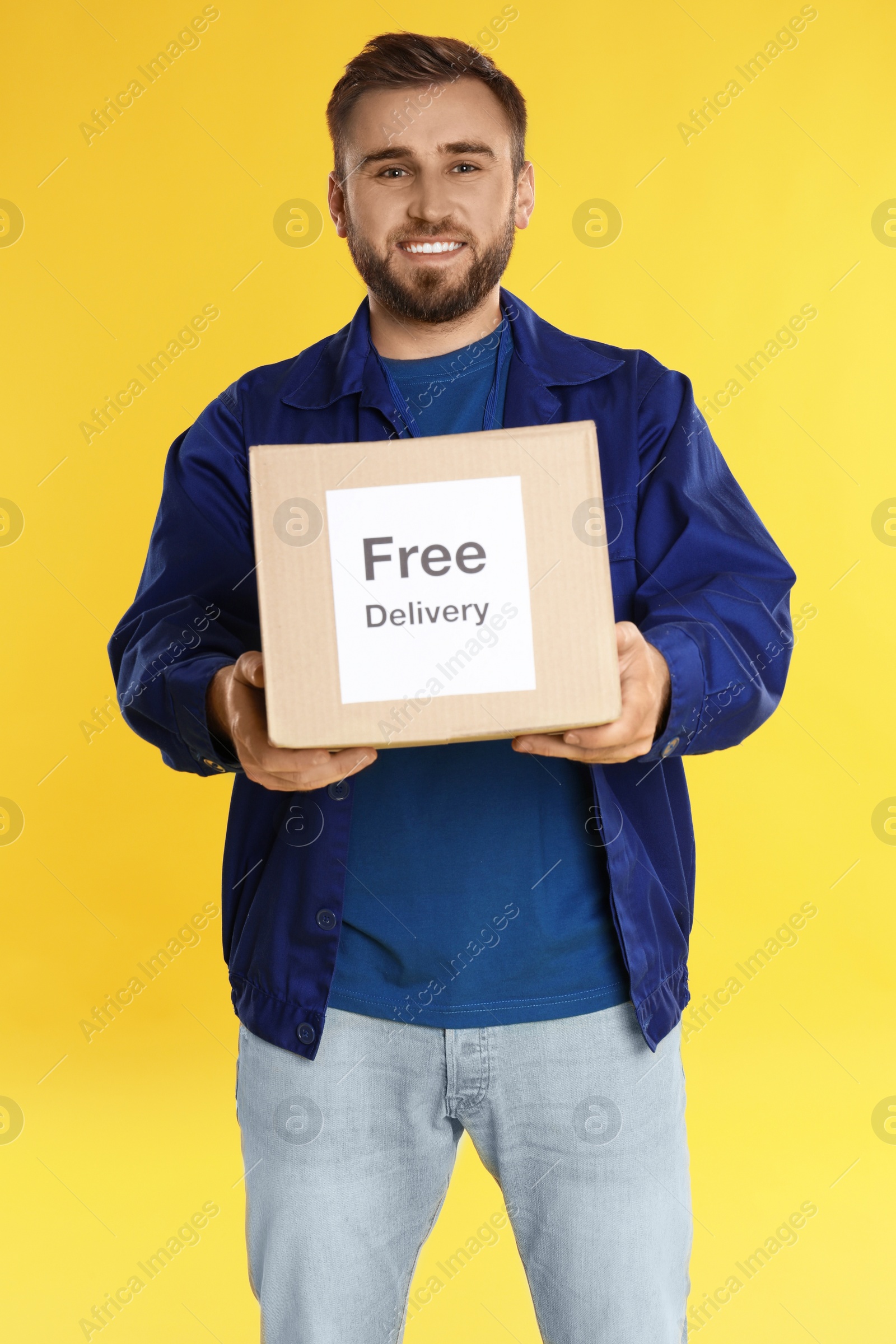 Photo of Male courier holding parcel with sticker Free Delivery on yellow background