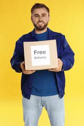 Photo of Male courier holding parcel with sticker Free Delivery on yellow background