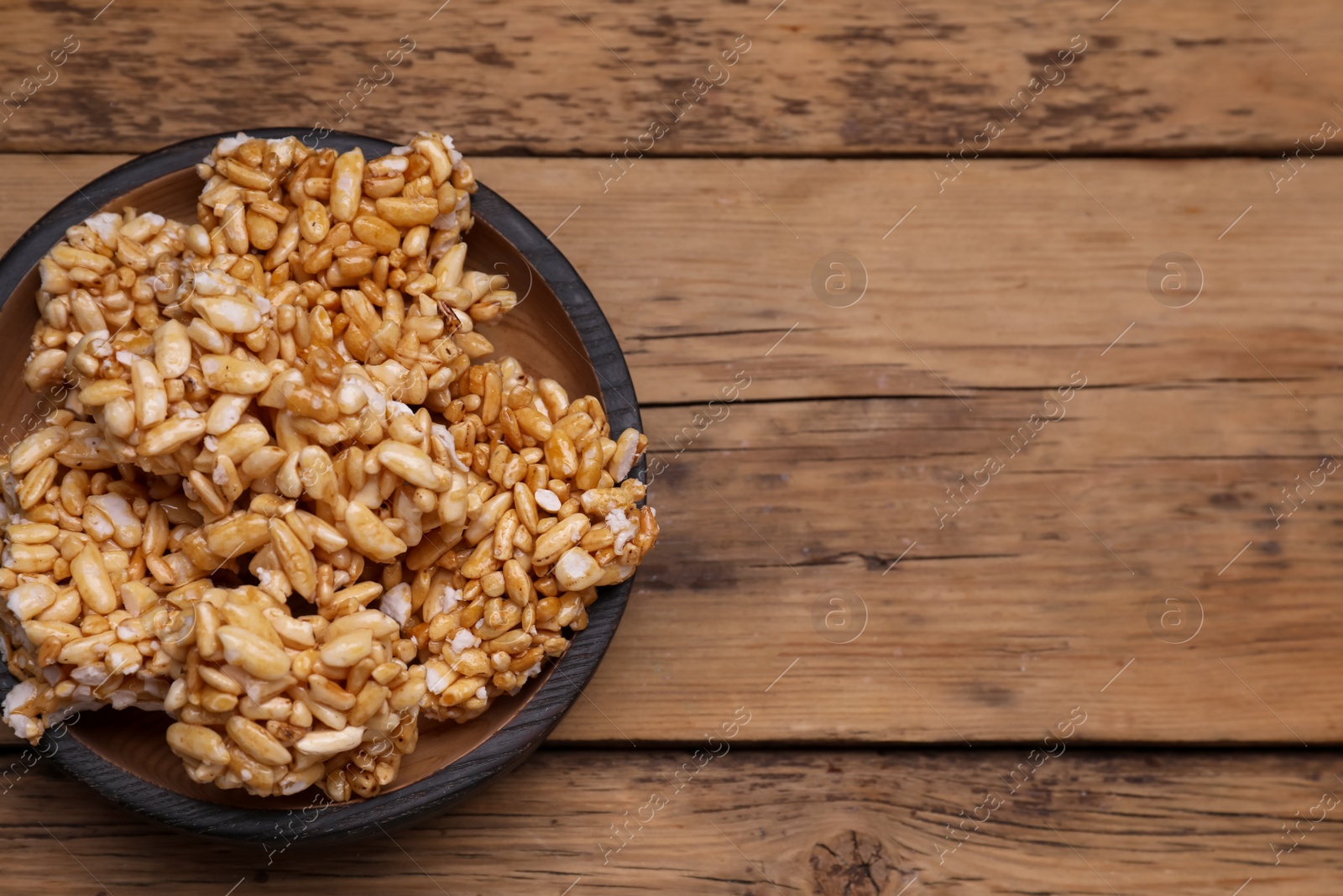 Photo of Bowl of puffed rice pieces (kozinaki) on wooden table, top view. Space for text