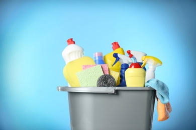 Photo of Bucket with different cleaning products and supplies on light blue background, closeup