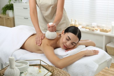 Young woman receiving herbal bag massage in spa salon