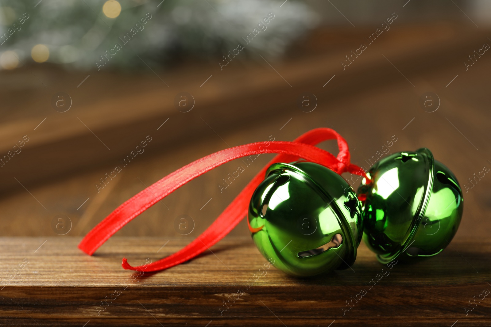 Photo of Green sleigh bells with red ribbon on wooden table, closeup