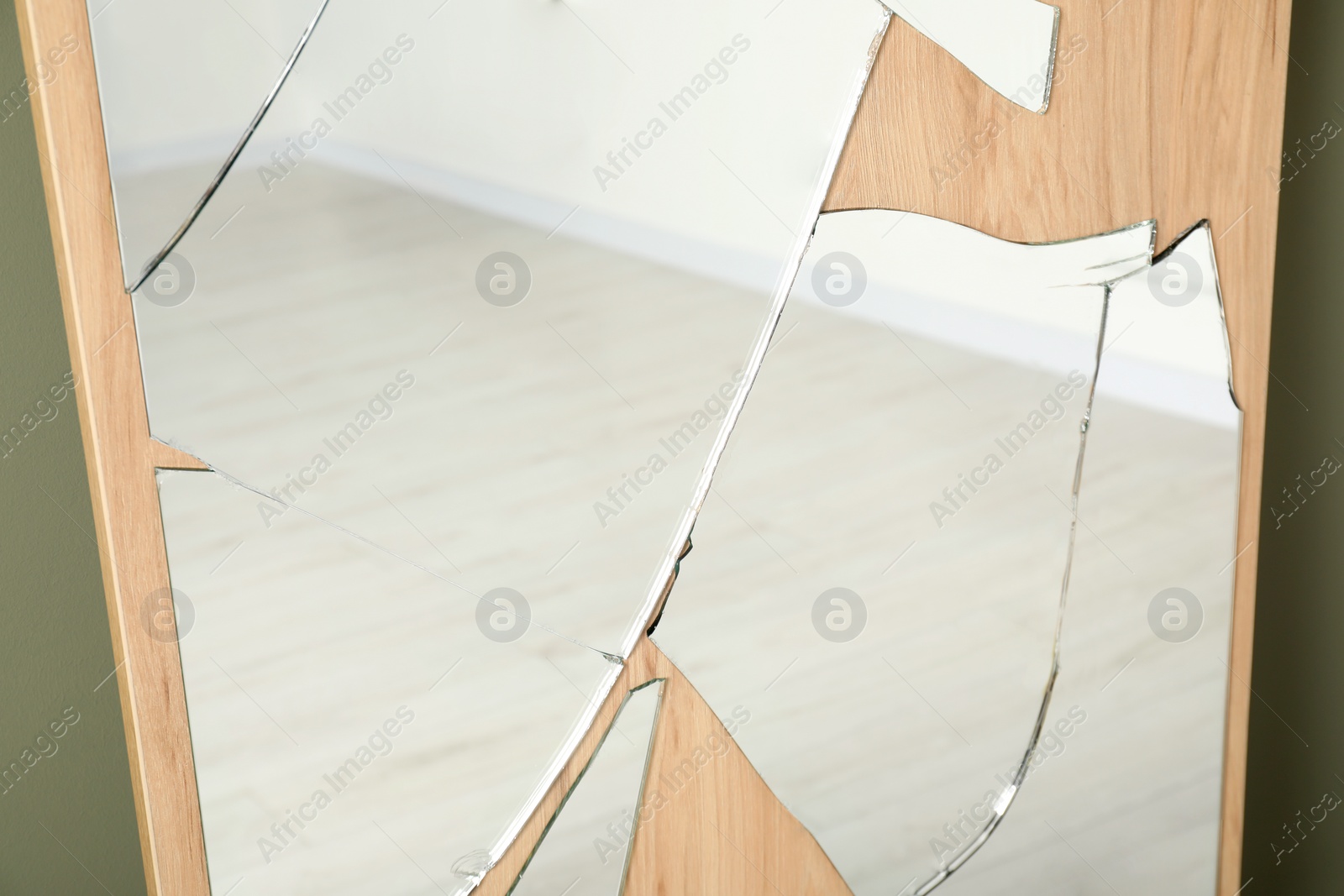 Photo of Broken mirror with many cracks near olive wall, closeup view