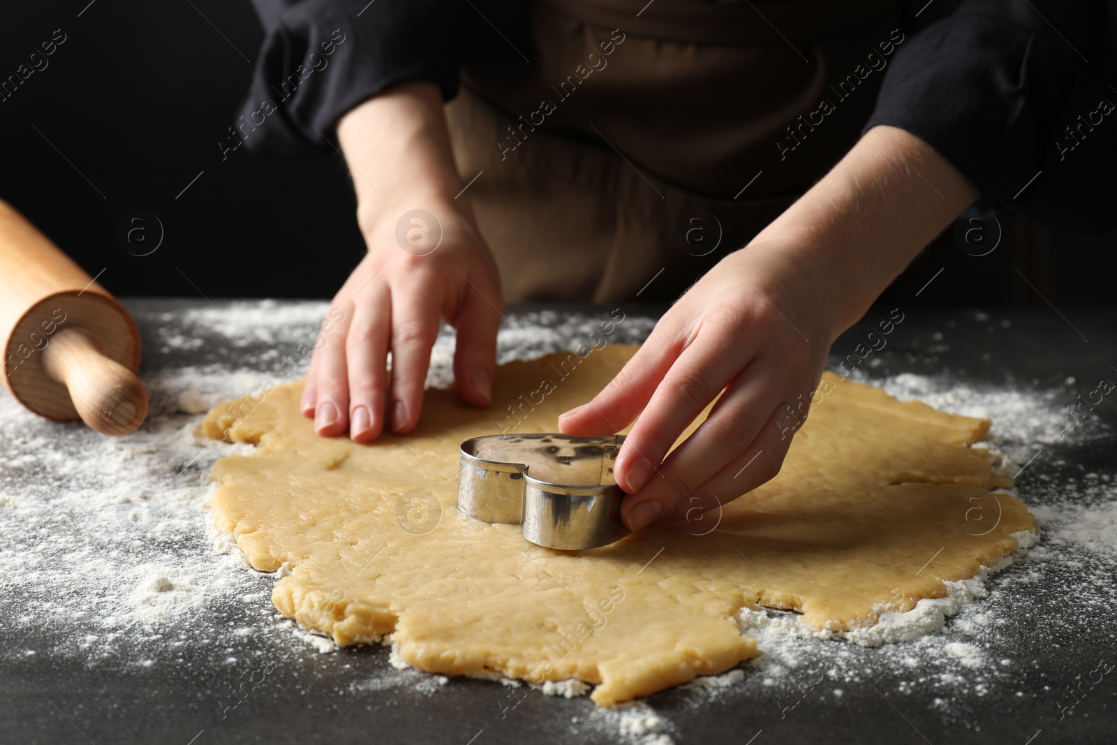 Photo of Shortcrust pastry. Woman making cookies with cutter at grey table, closeup