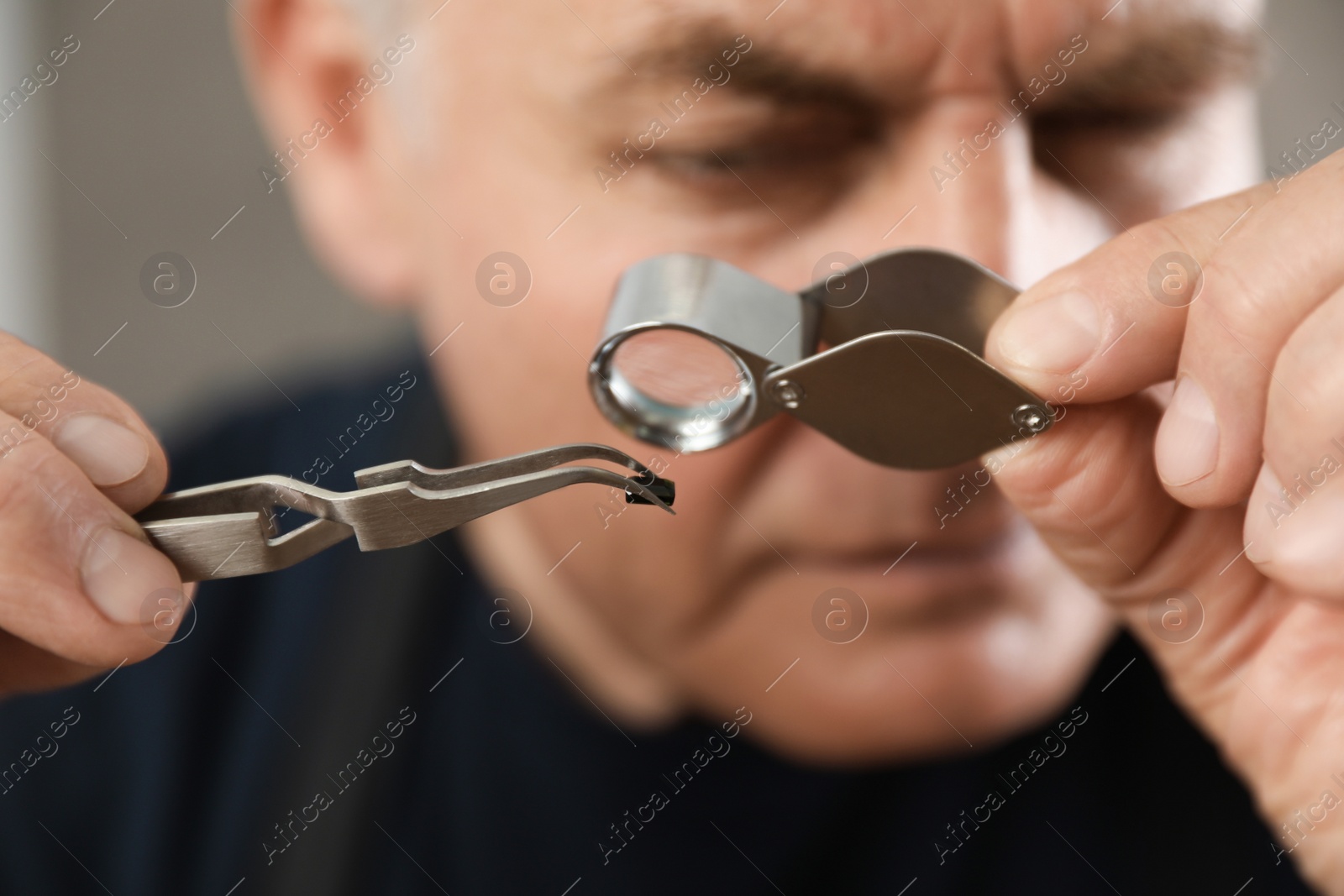 Photo of Male jeweler evaluating precious gemstone in workshop, closeup