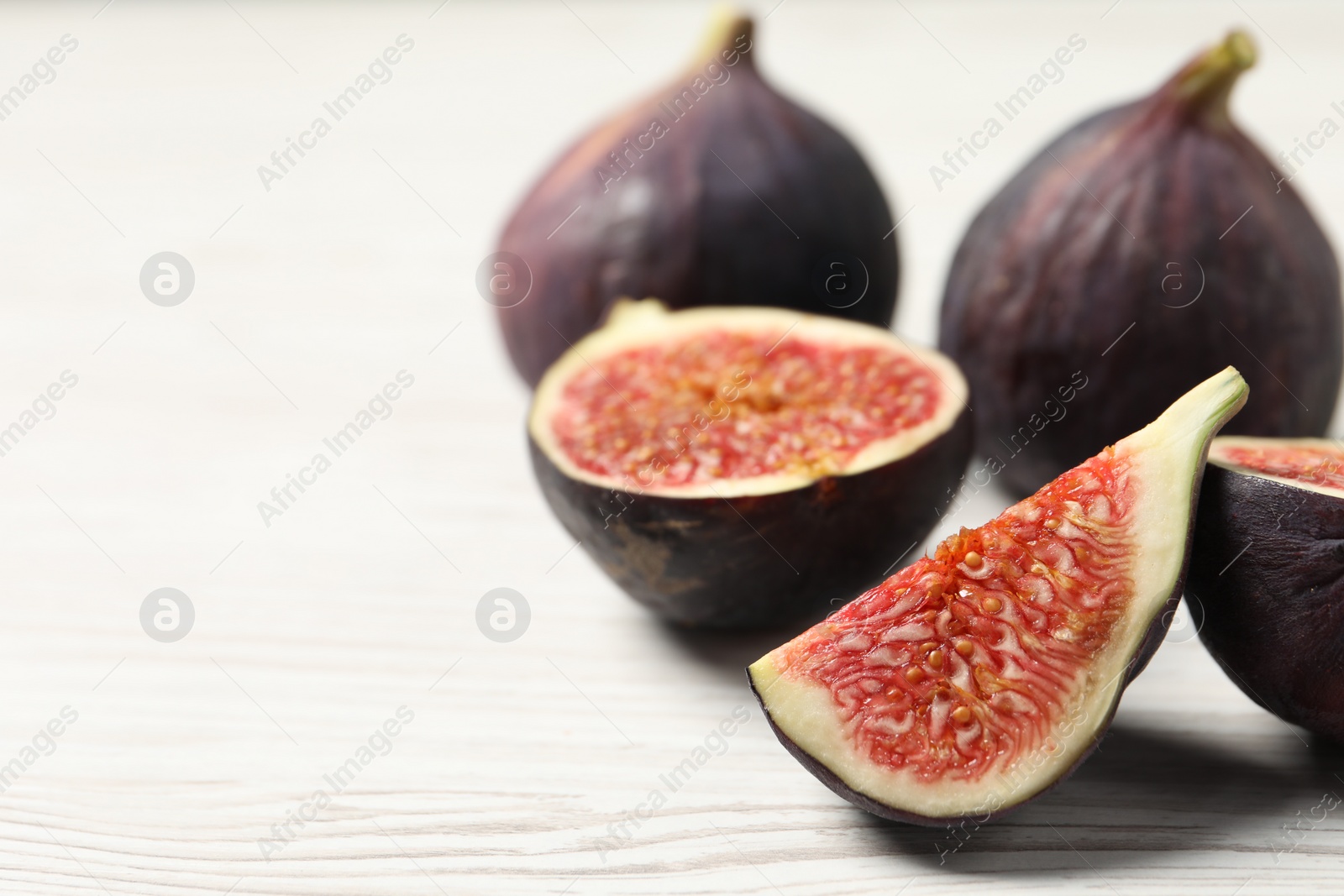 Photo of Whole and cut ripe figs on white wooden table, closeup. Space for text