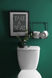 Decor elements, paper rolls and toilet bowl near green wall. Bathroom interior