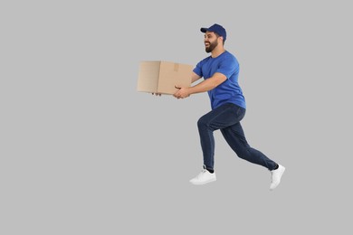Photo of Happy young courier running to deliver parcel on grey background, space for text