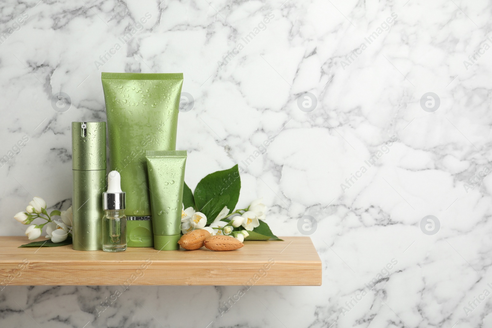 Photo of Set of cosmetic products, almond nuts and flowers on wooden shelf near white marble wall, space for text