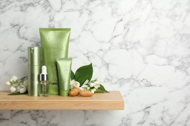 Photo of Set of cosmetic products, almond nuts and flowers on wooden shelf near white marble wall, space for text