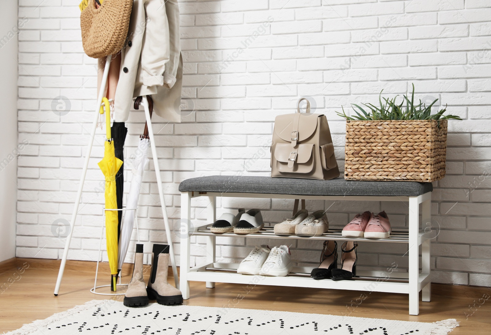 Photo of Stylish hallway interior with coat rack and shoe storage bench near white brick wall