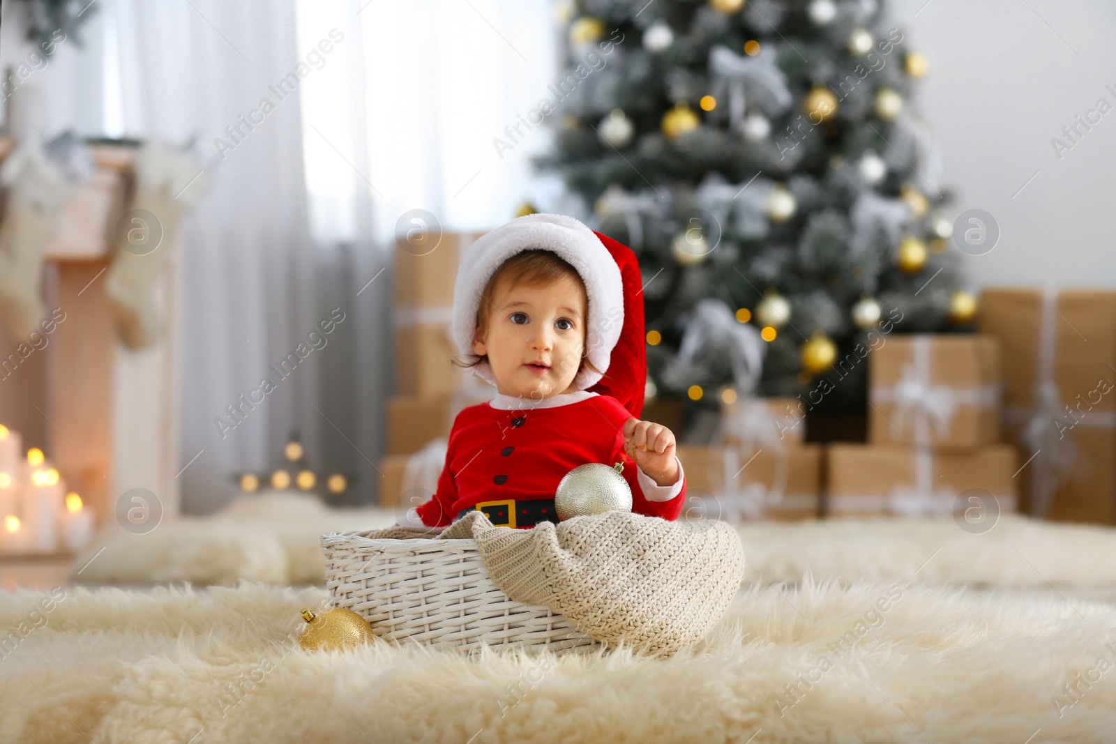 Image of Cute baby in Santa suit with Christmas ball at home