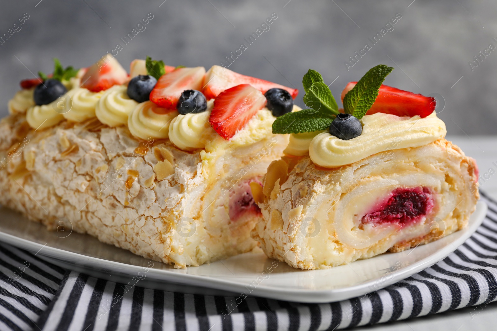 Photo of Tasty meringue roll with jam, cream, strawberry, blueberry and mint on plate, closeup