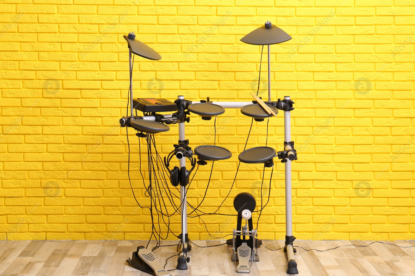 Photo of Modern electronic drum kit near yellow brick wall indoors. Musical instrument