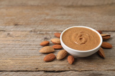 Photo of Delicious nut butter in bowl and almonds on wooden table. Space for text