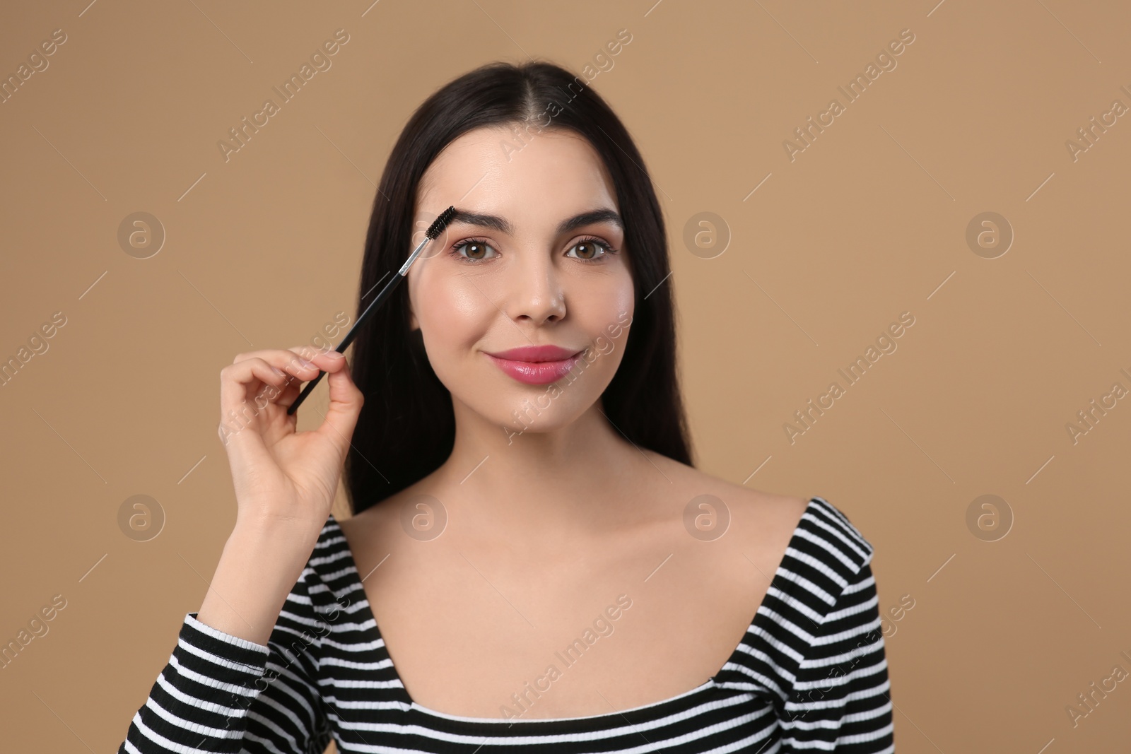 Photo of Woman applying makeup with eyebrow brush on light brown background