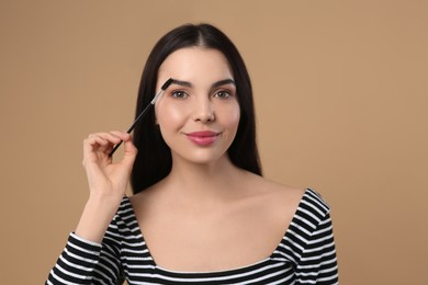 Woman applying makeup with eyebrow brush on light brown background