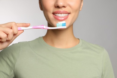 Photo of Woman holding toothbrush with paste on light background, closeup