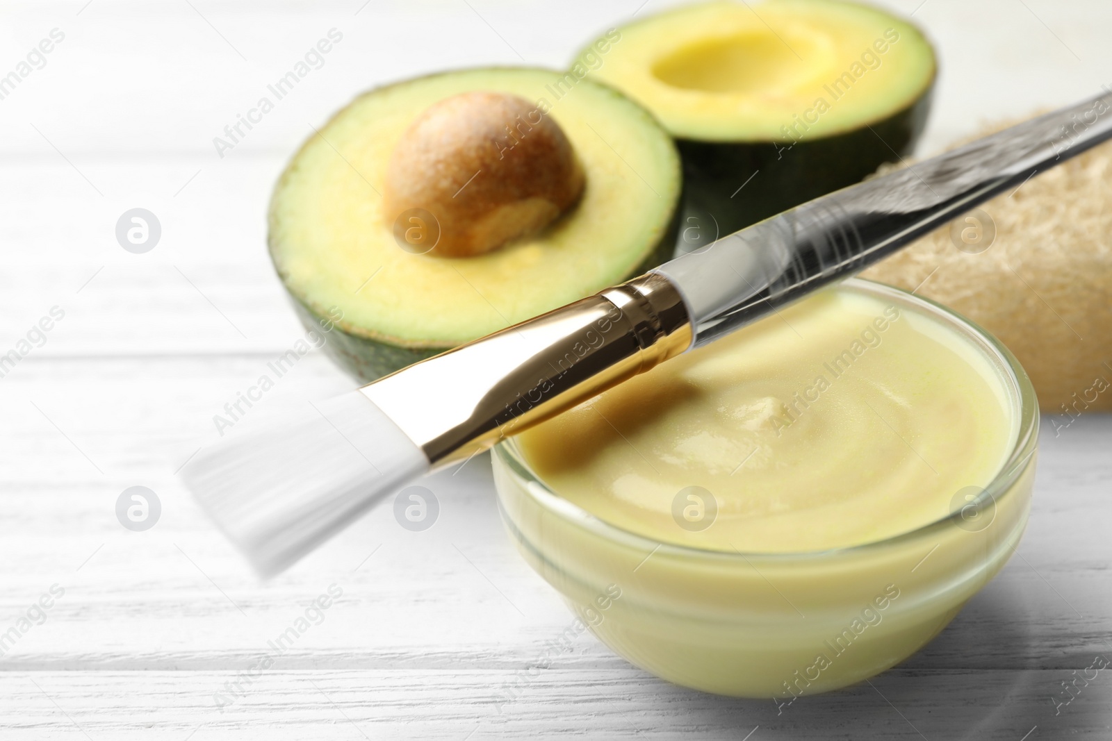 Photo of Handmade face mask in glass bowl and brush on white wooden table