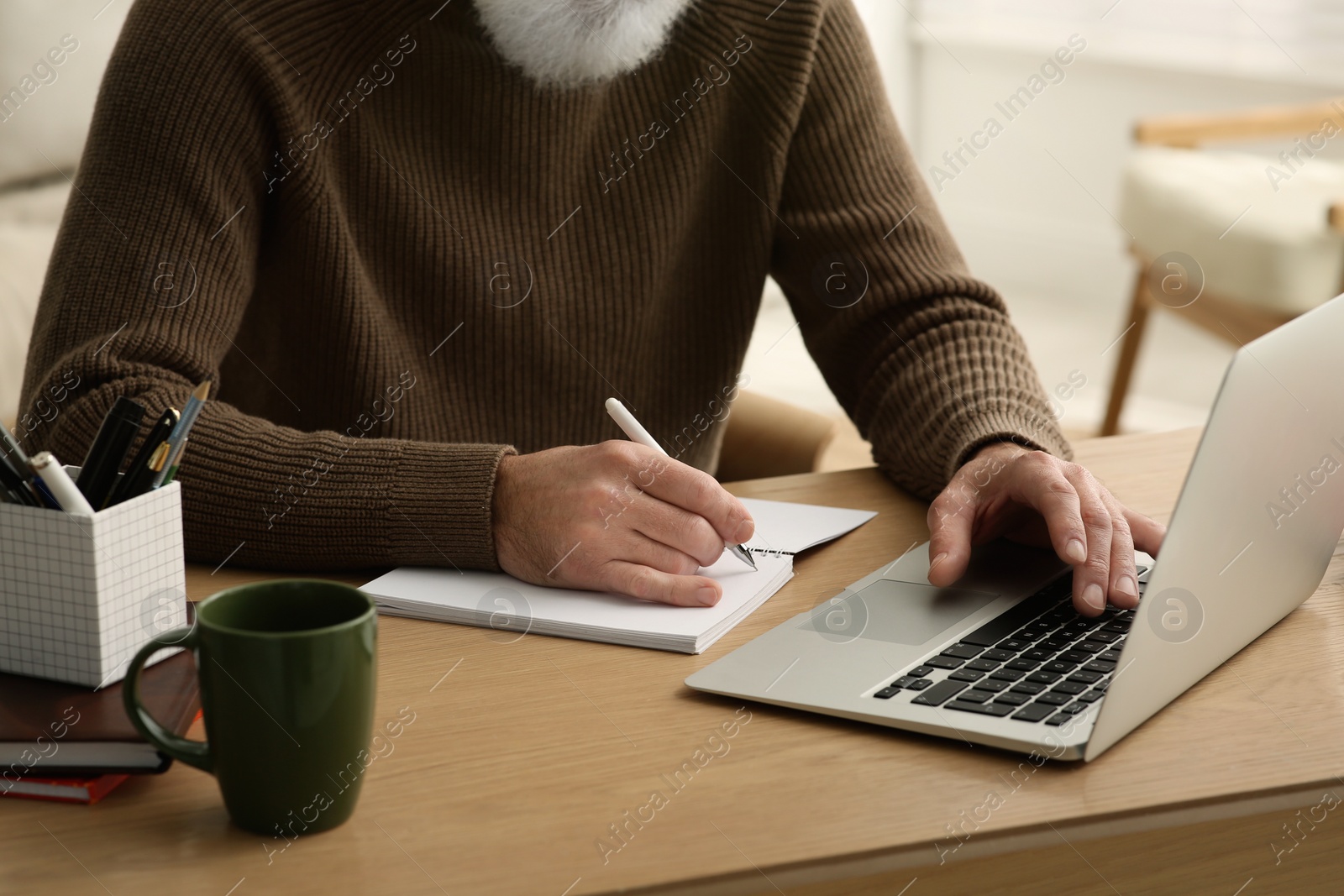 Photo of Man with laptop and notebook learning at wooden table indoors, closeup