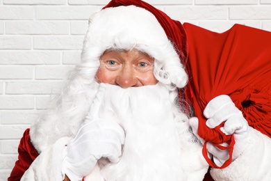 Photo of Authentic Santa Claus with bag full of gifts against white brick wall