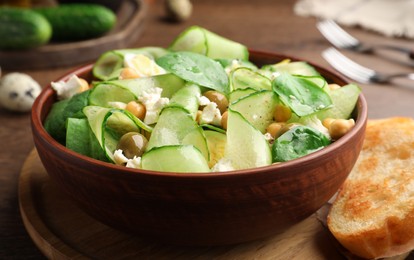 Photo of Delicious cucumber salad and toasted bread served on wooden table, closeup