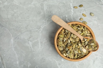 Photo of Bowl and spoon of raw pumpkin seeds on light grey marble table, top view. Space for text