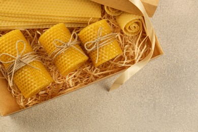 Photo of Beautiful yellow beeswax candles and sheets in box on light textured table, top view