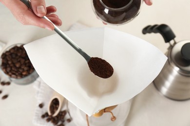 Making drip coffee. Woman adding ground coffee into paper filter at white table, closeup