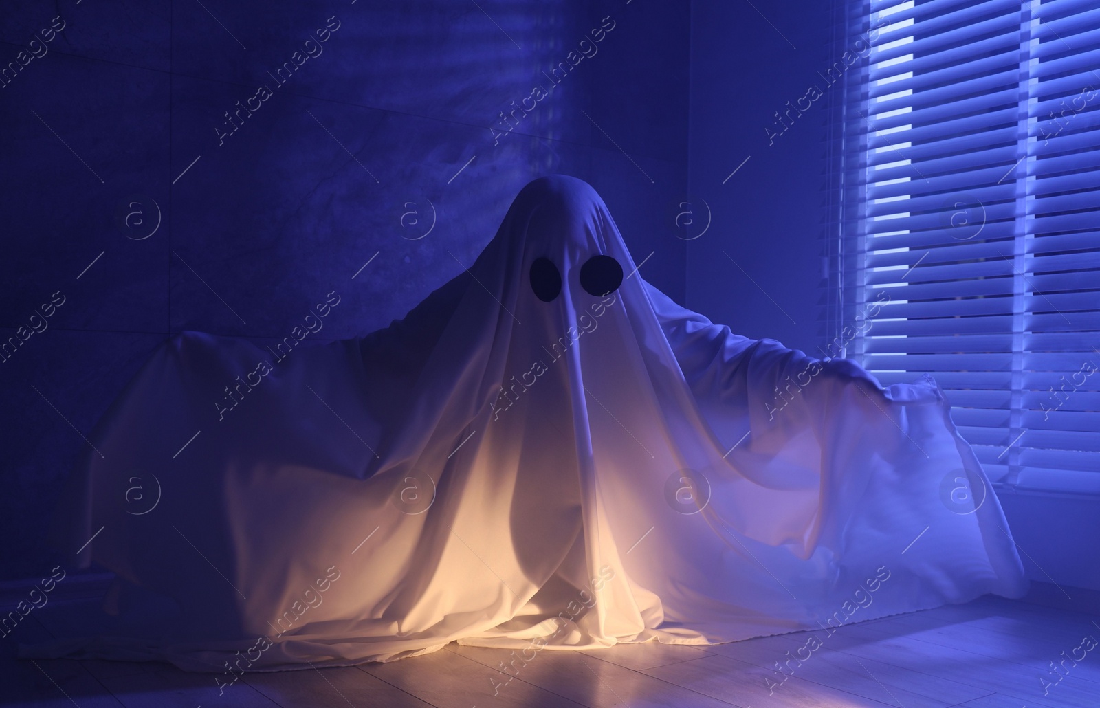 Photo of Creepy ghost. Woman covered with sheet near window in blue light