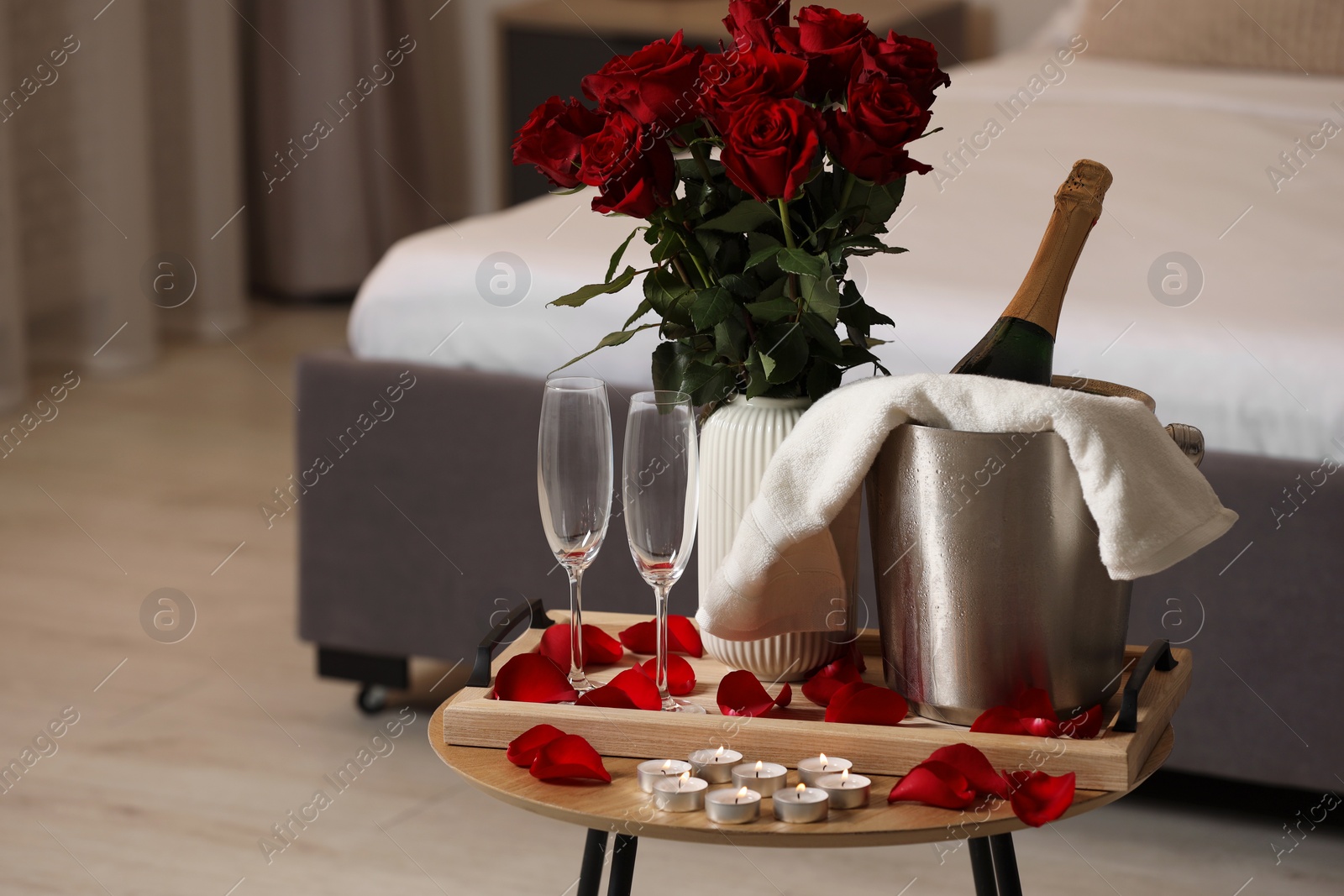 Photo of Honeymoon. Sparkling wine, glasses and bouquet of roses on wooden table in room. Space for text