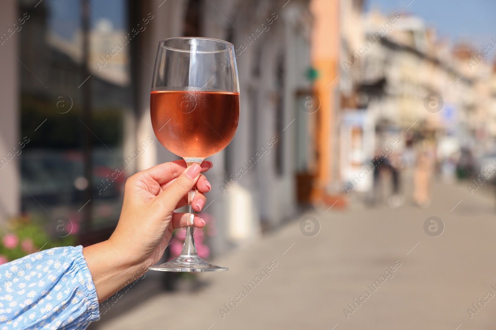 Photo of Woman holding glass of rose wine outdoors, closeup. Space for text