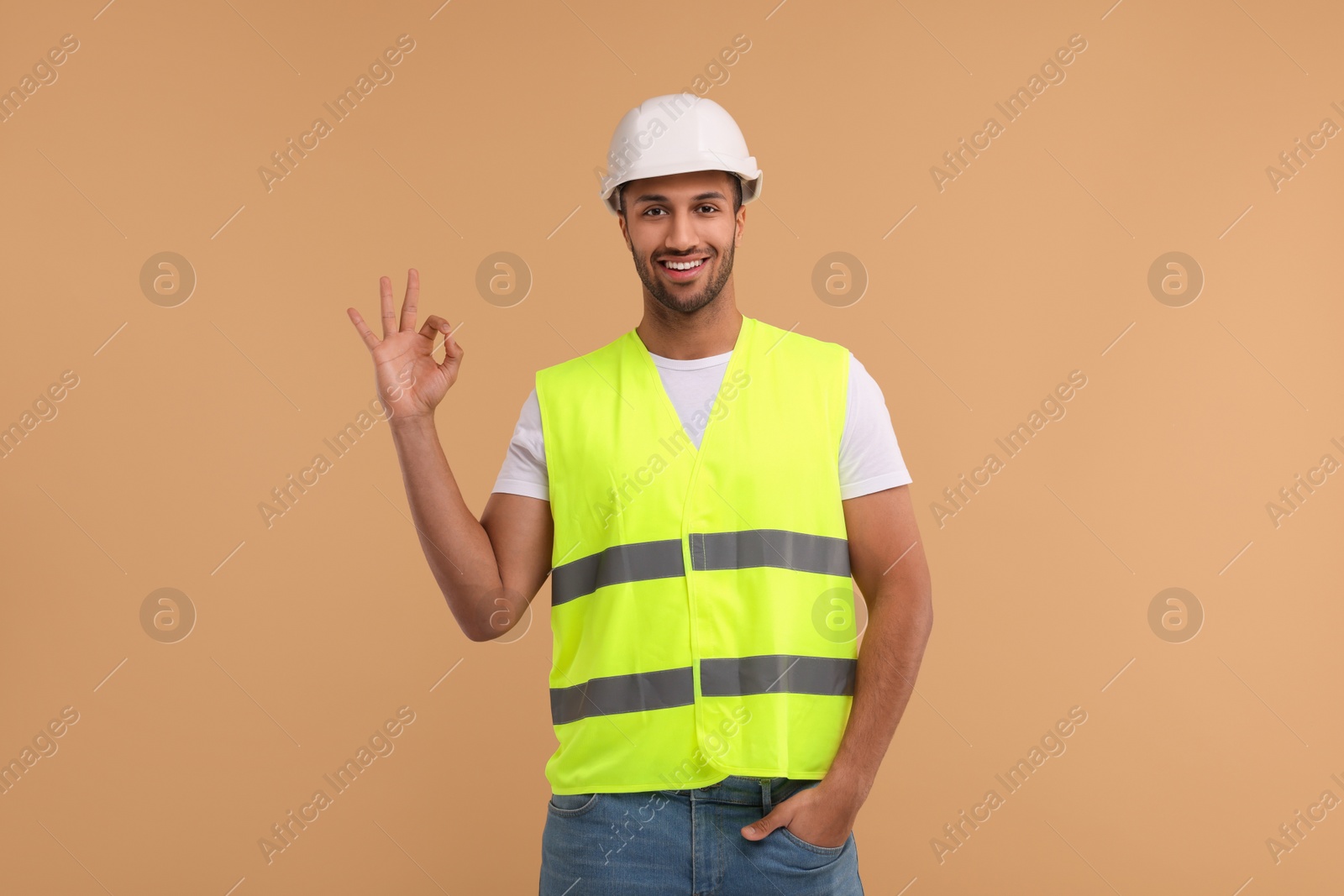 Photo of Engineer in hard hat showing ok gesture on beige background