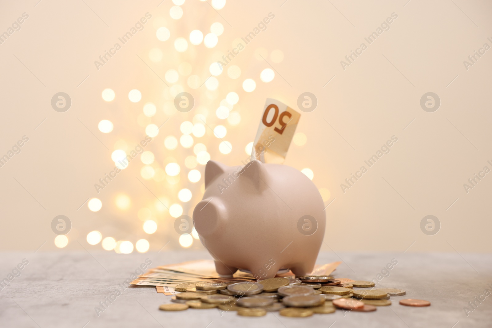 Photo of Piggy bank with euro banknote and coins on grey table against blurred lights