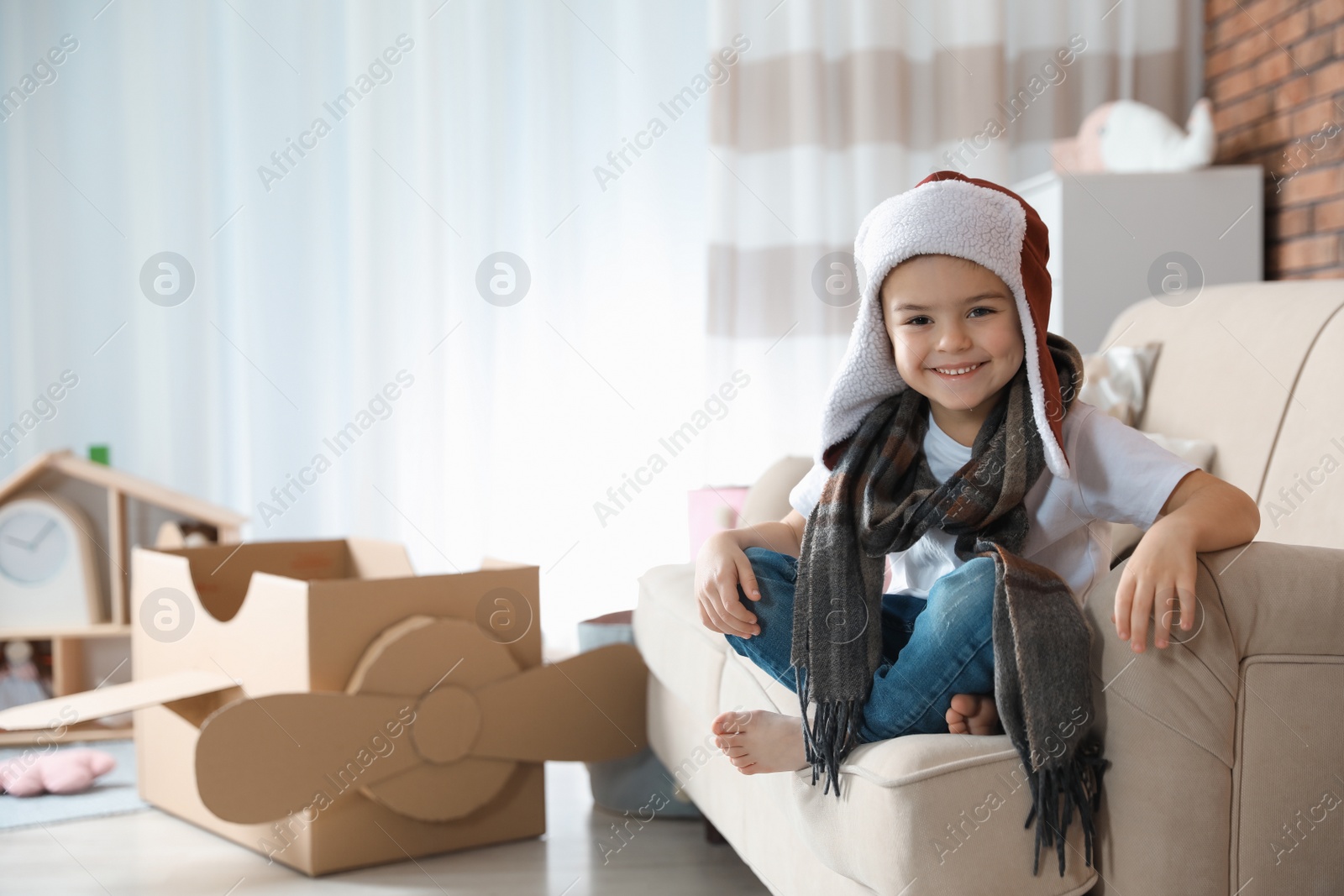 Photo of Cute little boy in pilot hat and blurred cardboard airplane on background. Space for text