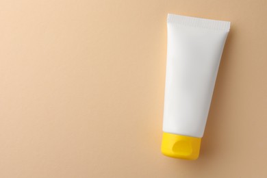 Tube of face cream on beige background, top view. Space for text