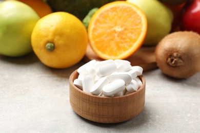 Dietary supplements. Pills in bowl and food products on grey table