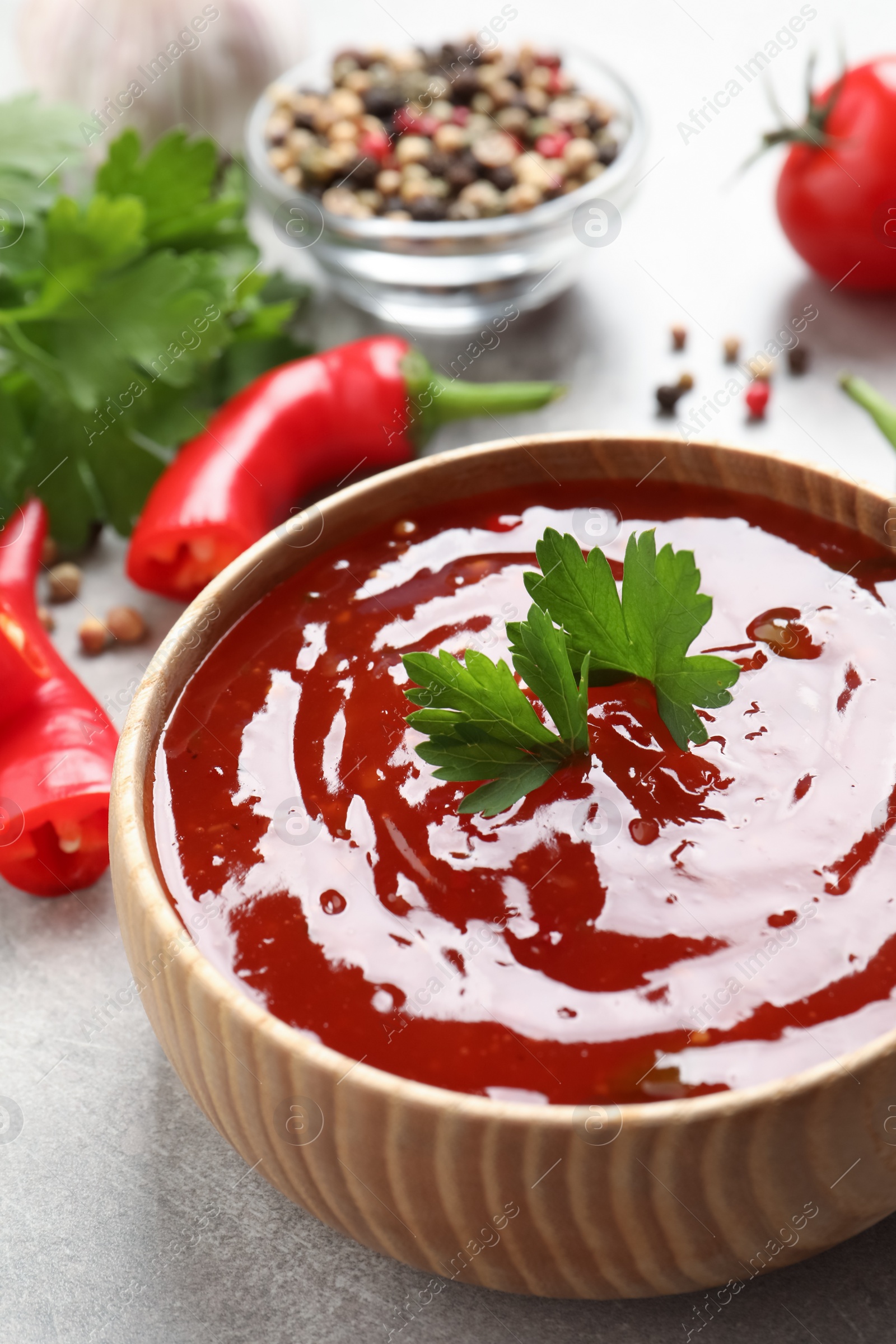 Photo of Spicy chili sauce with parsley in wooden bowl on light grey table