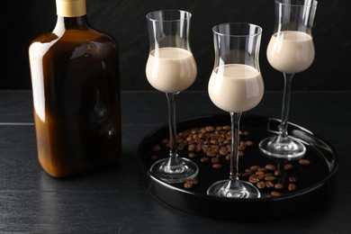 Coffee cream liqueur in glasses, bottle and beans on black wooden table