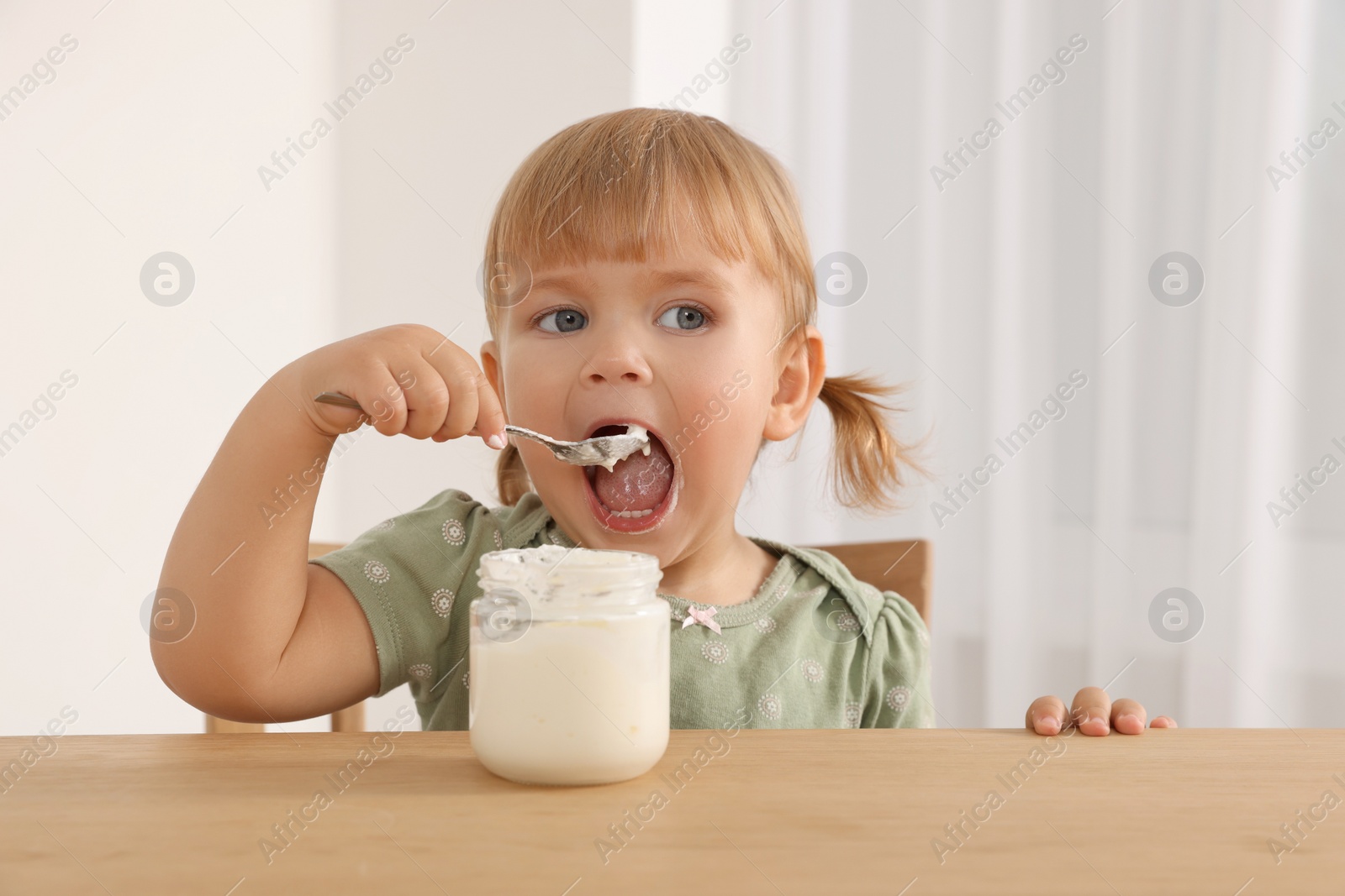 Photo of Cute little child eating tasty yogurt with spoon at wooden table indoors