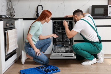 Photo of Woman discussing with repairman near dishwasher in kitchen